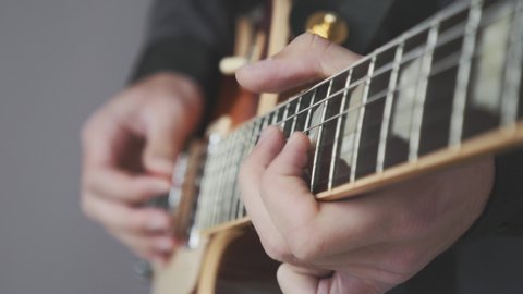 Male hands playing on electric guitar close up. Fingers on guitar fretboard holding pick and playing chords and solo. Musical instruments concept