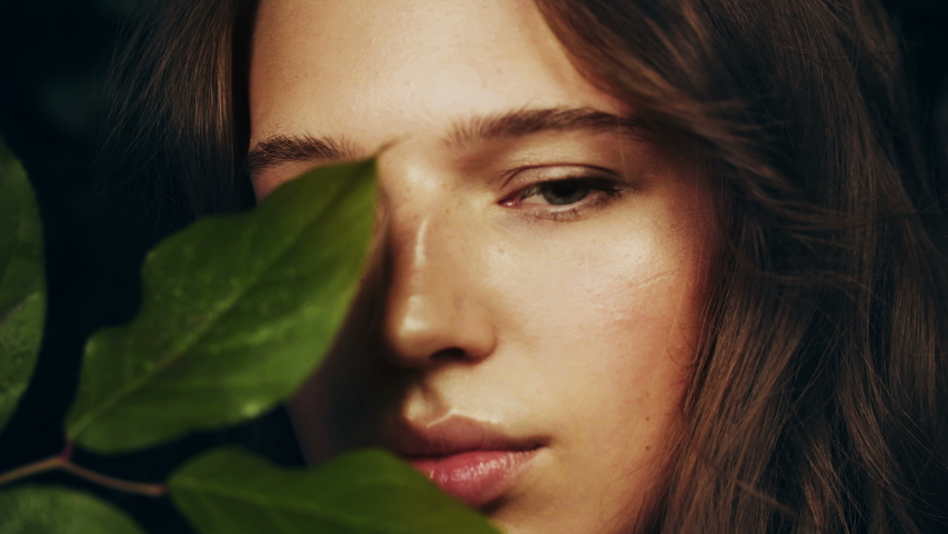 Face of beautiful girl with green leaves of flowers and plants. Natural cosmetics and skin care. Exotic flower. Perfume Advertising. 