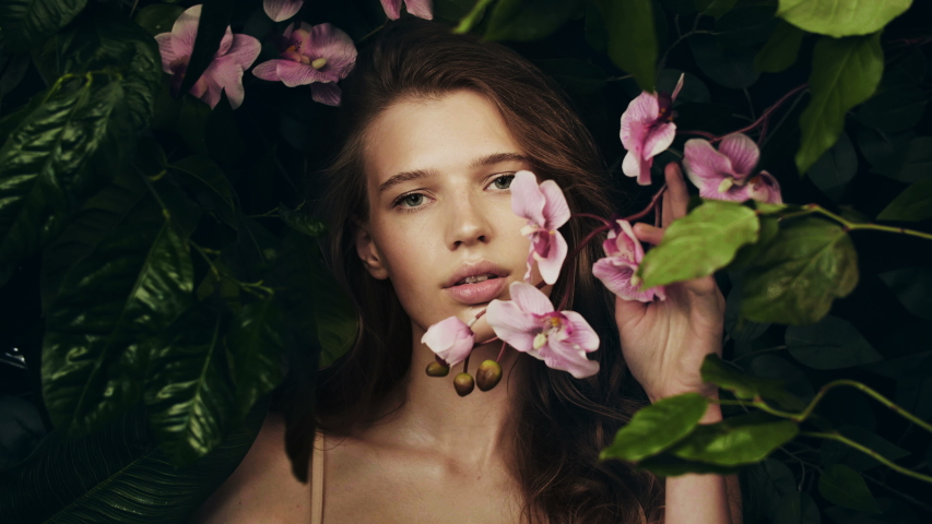 Beautiful girl among the plants and flowers of the archidea. Natural cosmetics and skin care. Exotic flower. Girl in jungle. Perfume Advertising.