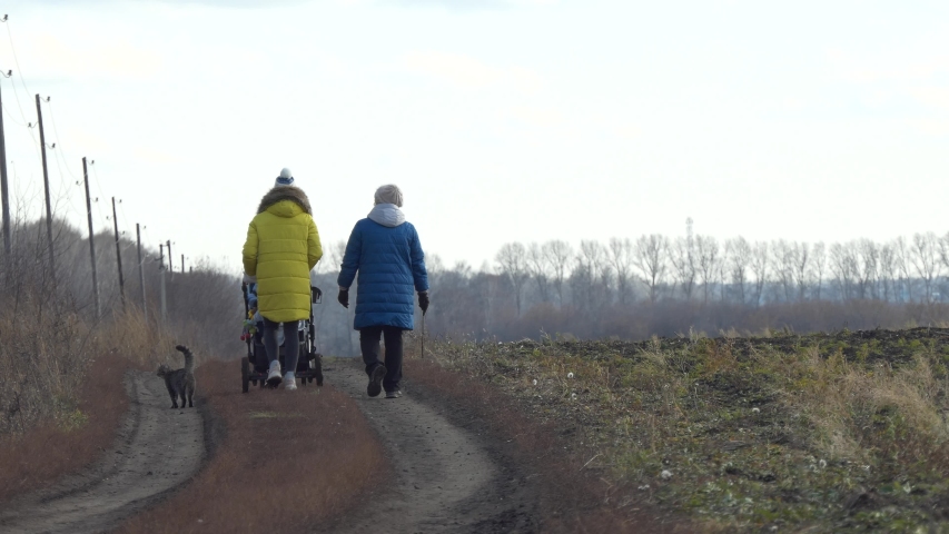 Women with a child in a pram and a cat are on a rural road. Autumn.