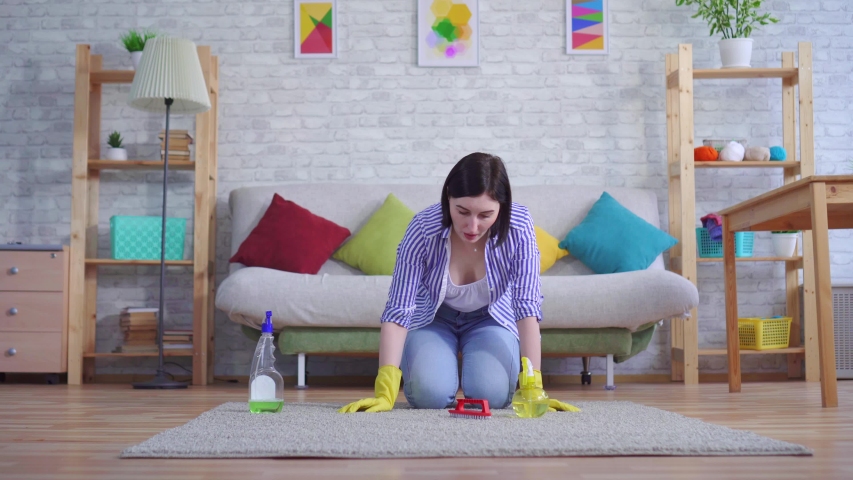 young woman in gloves with discontent cleans the carpet with her hands