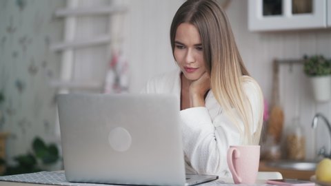 Young woman uses laptop for work at home. Girl looking at screen of computer