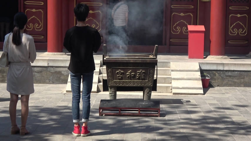 Static footage of two people praying at Lama Temple located in Dongcheng District Beijing China the building and artwork are a combination of Han Chinese and Tibetan styles 4k high resolution quality