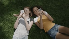 Smiling girls laying on grass using cell phones / Provo, Utah, United States