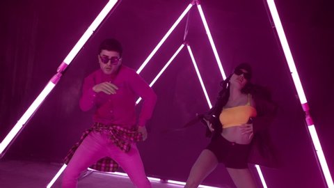 Professional Hip Hop break dancers . Stylish young couple dancing with real strobe lights . Against lilac background with triangle shape of led lights . Real decoration . Showing heart by fingers .