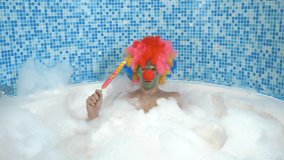 Cute clown man in a bathtub with plentiful foam eats a lollipop on a stick. humorous concept. - Powered by Shutterstock - Get 15% off with code: PIKWIZARD15
