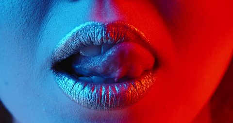 Sensual girl with bright glowing lipstick seductively licking her lips in neon light - nightlife, nightclub concept extreme close up shot 4k footage