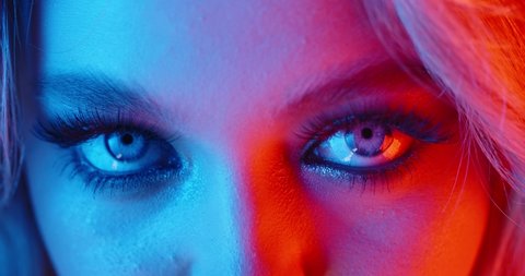Sexy blonde girl with glowing makeup giving a seductive look in neon light - nightlife, nightclub concept 4k footage extreme close up shot