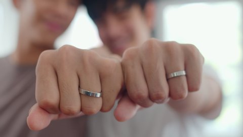 Portrait Young Asian Gay couple feeling happy showing ring at home. Asia LGBTQ+ men relax toothy smile looking to camera while hug in modern living room at house in the morning concept. Close up Shot.