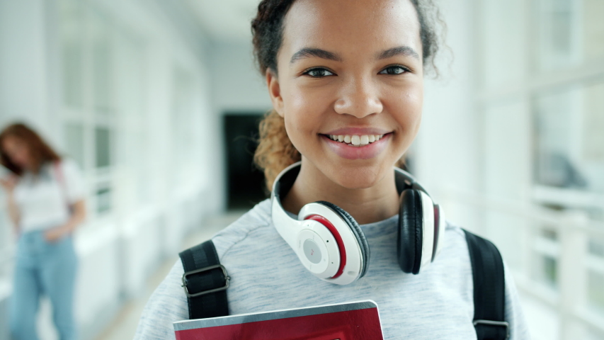 Close-up portrait of young African American lady student smiling standing in university hall alone looking at camera. People, youth and education concept.