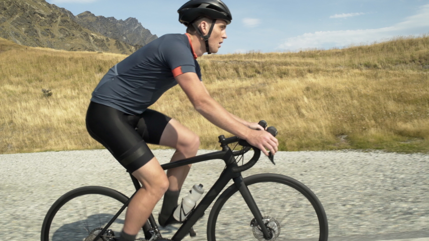 Confident fit Caucasian male cyclist climbing up biking mountain road outdoor The Remarkables Lake Wakatipu South Island Otago New Zealand