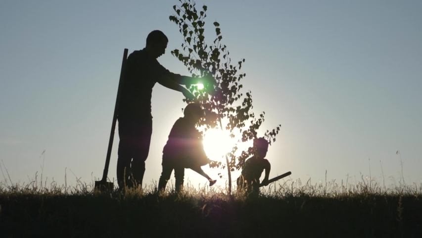 Agriculture. Farmer with his family is planting tree. Family silhouette. Agriculture concept. Happy family of farmer. Silhouette of father and two children planting and watering tree in park at sunset Royalty-Free Stock Footage #1040473283