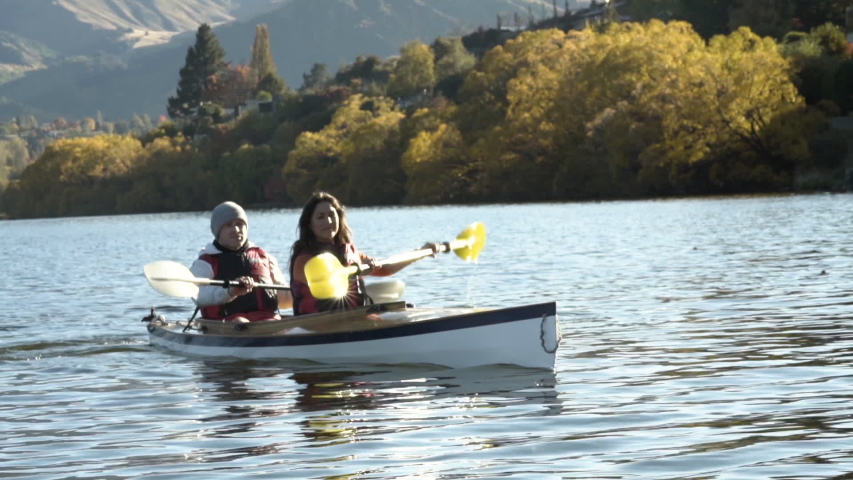 Young Caucasian couple in the kayak paddling spending their vacation enjoying togetherness in Autumn sun flare Lake Wakatipu New Zealand