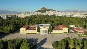 Aerial drone video of renovated public neoclassic building of Zappeion used for events and meetings in the National Gardens of Athens and Lycabettus hill aligned at the background, Greece