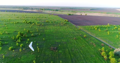 Hang glider flight in sunset time over green and yellow fresh spring fields. Aerial top view. Taken with drone.
