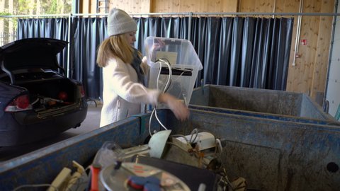 KIRKKONUMMI, FINLAND - OCT 04, 2019: A young woman puts old appliances in a dumpster in sorting station HSY - center for sorting and recycling of waste, household, construction waste and electrical