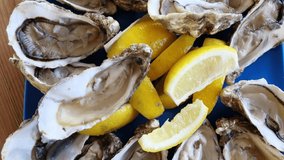 Fresh Oysters close-up on green plate, served table with oysters, lemon. Table top view. Healthy sea food. Fresh raw oyster dinner in restaurant. Gourmet food. Rotation. 4K UHD video
