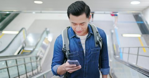asian young man use 5g smartphone on the escalator in metro station