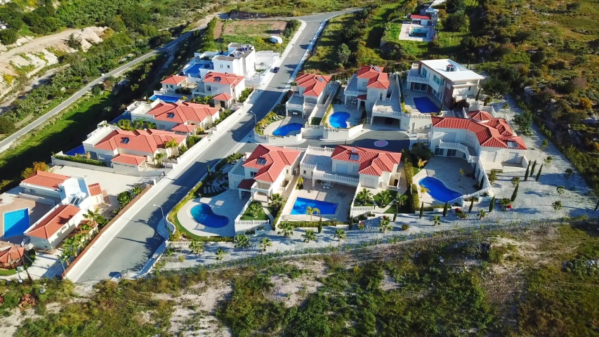 Paphos, Cyprus. Aerial view of the houses and the landscape. Beautiful villas with swimming pool, surrounded by palms, flowers and picturesque hills. Was filmed at sunny day 