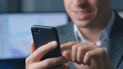 Close-up of a successful businessman in a suit is using a smartphone in the office at the workplace. Man uses the application on a mobile phone, office on the background