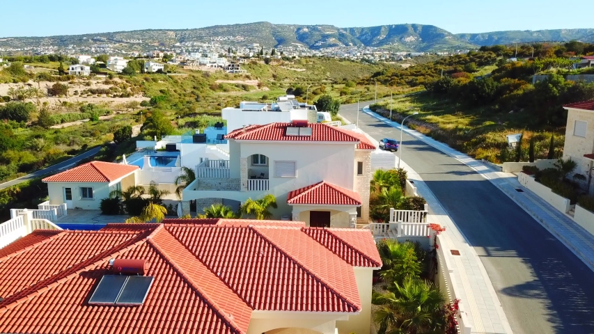 Paphos, Cyprus. Drone flying over houses and the landscape. Beautiful villas with swimming pool, surrounded by palms, flowers and picturesque hills. Taken by drone at sunny day 