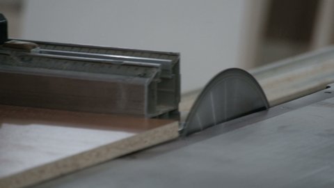 The worker saws off the edge of the chipboard on a machine with a circular saw. Close-up. Furniture manufacture. The video contains real production sound and noise.