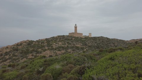 Lighthouse on the top of the hill among mediterranean vegetation on a cloudy and windy day at Saint Peter island in sardinia region, Italy