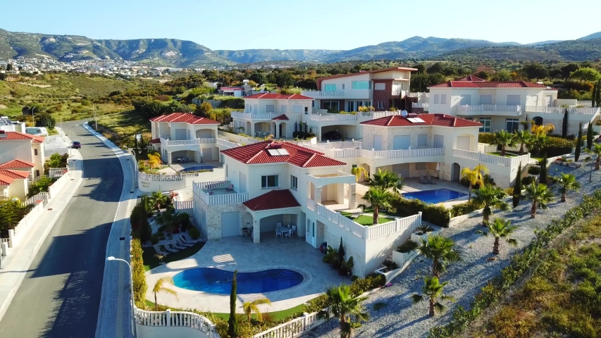 Aerial top view of the houses and the landscape in Paphos, Cyprus. Beautiful villas with swimming pool, surrounded by palms, flowers and picturesque hills. Was filmed at sunny day 