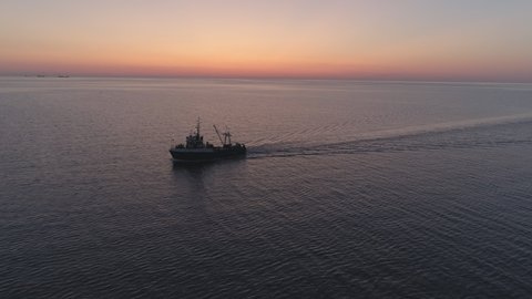 Fishing boat trawler ship sailing on sea after sunset aerial shot