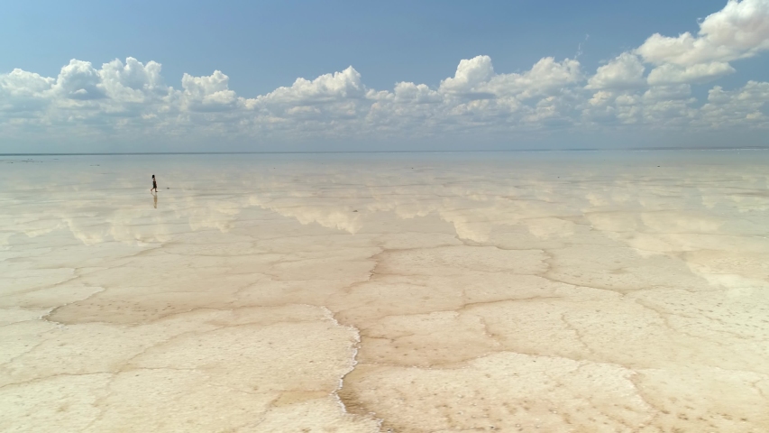 Mysterious place Russia salt lake Elton boundless expanse brine crust many cracks pattern. Man walks through transparent water beautiful clouds reflected. Another planet universe afterlife Martian Royalty-Free Stock Footage #1040525156
