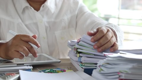 Education and business concept. Asian teacher hands is searching for student's homework assignments archive with colorful papers on table to make a check and inspect. Stack of paperwork and reports. 