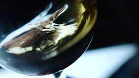 Waving gold white wine in a glass on defocused dark background . Beautiful stock footage for wine commercial . Close up video of wine mixing process inside goblet . Shot on ARRI ALEXA in Slow Motion .