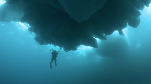 a scuba diver photographs moodful scenery under impressive icebergs