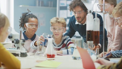 Elementary School Science Classroom: Enthusiastic Teacher Explains Chemistry to Diverse Group of Children, Little Boy Mixes Chemicals in Beakers. Children Learn with Interest