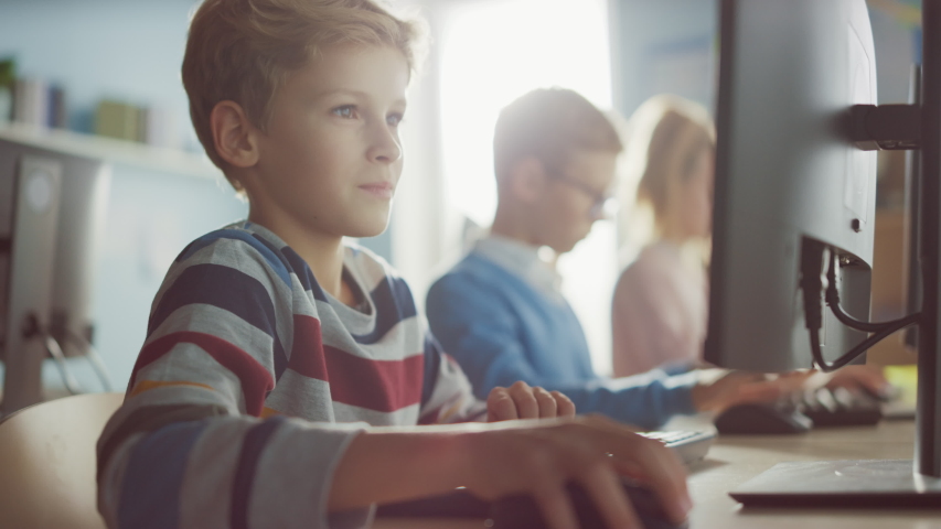Elementary School Classroom: Smart Boy Uses Personal Computer, Learning How to Use Internet Safely, Programming Language for Software Coding. Schoolchildren Getting Modern Education. Portrait Shot Royalty-Free Stock Footage #1040541497