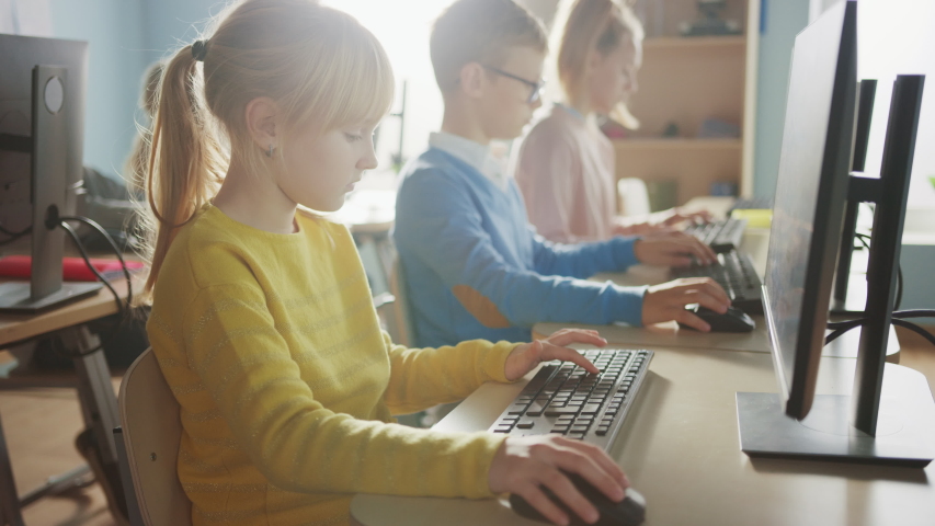 Elementary School Computer Science Classroom: Cute Little Girl Uses Personal Computer, Learning Programming Language for Software Coding. Schoolchildren Getting Modern Education. Side View Portrait Royalty-Free Stock Footage #1040541530