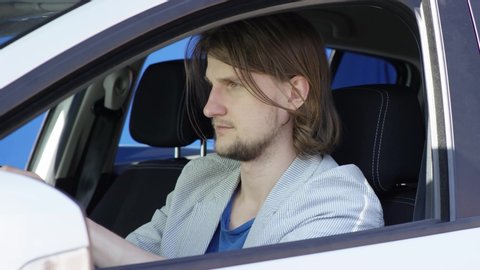 Brunette man in casual clothes is driving car with greenscreen background. He is sitting in his white car with the bluesceen background. He fastens his seat belt