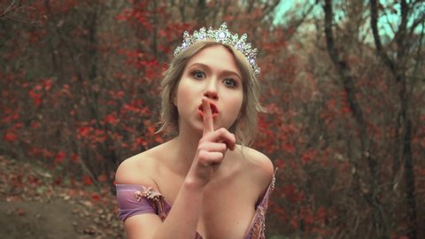 beautiful princess in crown puts finger to her lips and with gesture orders everyone to be silent. Cute queen's commands to close their mouth and not make noise. Attractive pretty face. Autumn nature