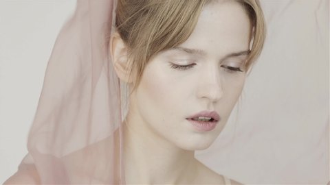 Girl's face on background of fluttering chiffon pink fabric. Gentle perfume. Nude makeup. The natural beauty of the girl. In studio. Slow motion fabric in wind. 