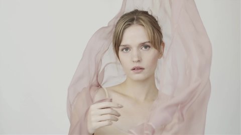 Girl on background of fluttering chiffon pink fabric. Gentle perfume. Nude makeup. The natural beauty of the girl. In studio. Slow motion fabric in wind.