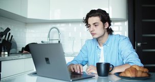 Young man working over laptop in the kitchen at breakfast