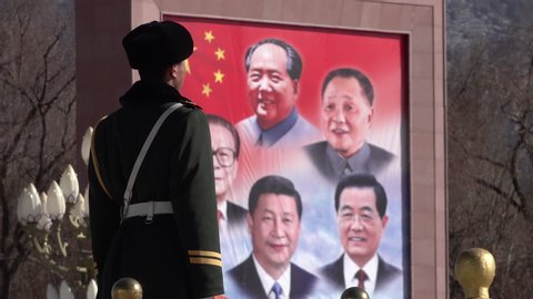 LHASA, TIBET – JANUARY 2019: Soldier of the Chinese liberation army stands guard at main square in Lhasa in Tibet, with political billboard (showing current and former Chinese presidents) 