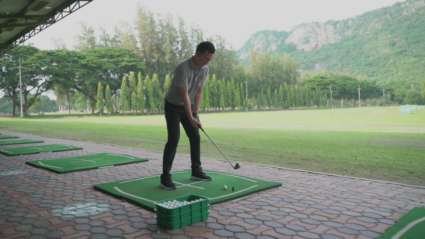 Young man takes a golf swing at a driving range 