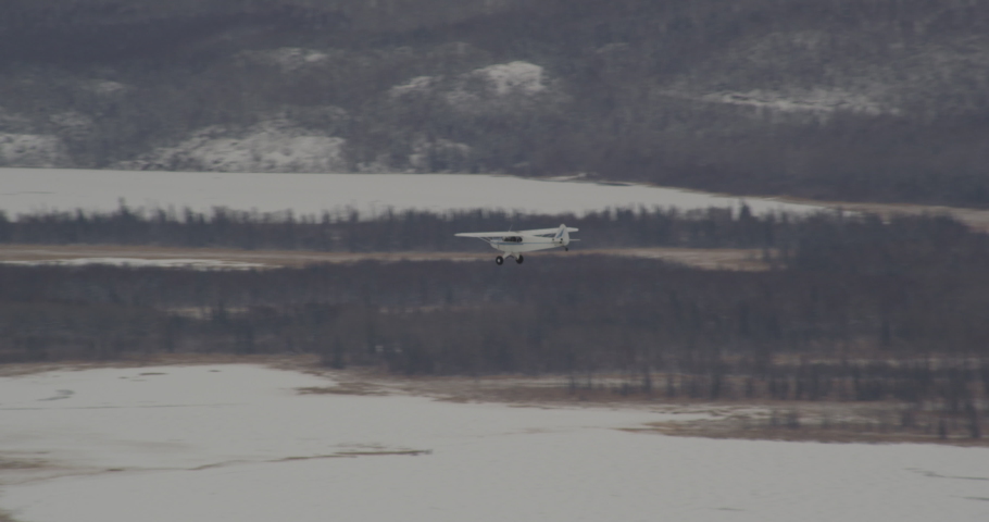 Aerial helicopter shot, zoom in on small blue and white airplane flying over vast Alaskan mountain valley and over snowy tundra, drone footage