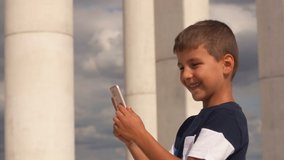 Happy smiling boy looks at the screen of a mobile phone against the background of beautiful columns