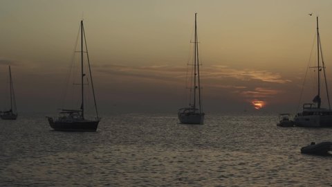 Many yachts in a bay on Formentera island. Incredible sunset in Cala Saona bay. Silhouettes of unrecognizable people on yachts