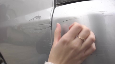 frustrated girl examines fresh scratch on fender and bumper of her car, hand close-up