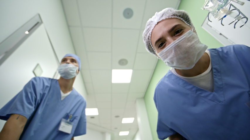 POV shot of patient of female nurse wheeling IV drip and talking as male ward assistant pushing stretcher along hospital corridor Royalty-Free Stock Footage #1040591324