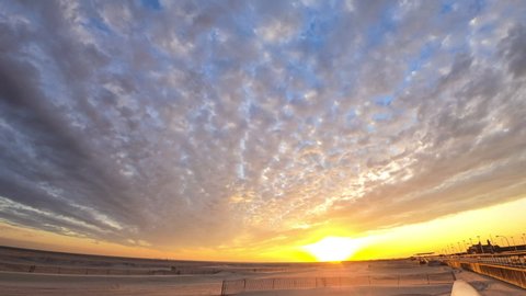 Time lapse of colorful high level clouds racing across the sky over a beach as the sun sets below the horizon. 