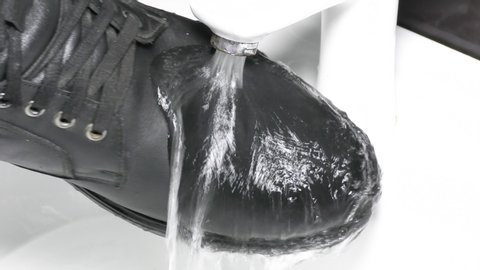 Stream of water falls on waterproof leather boots and rolls off the surface. Extreme close up 4k UHD video. Innovative shoe protection against water
